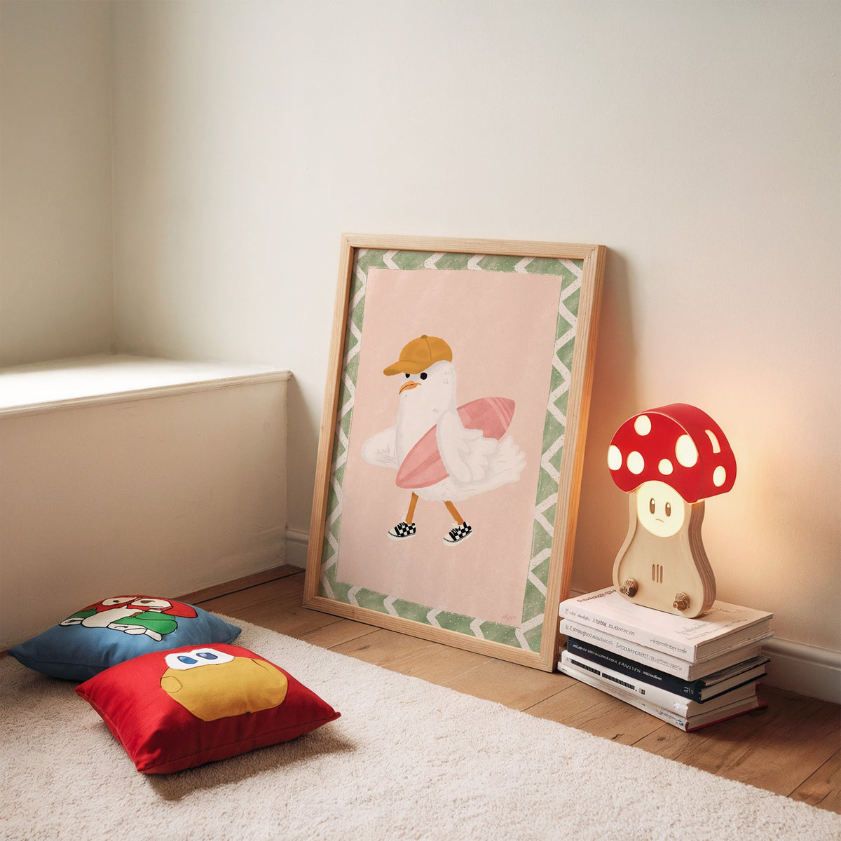 Surfer seagull with pink surfboard nursery print in an oak frame leaning on a rug beside a mushroom lamp and floor cushions