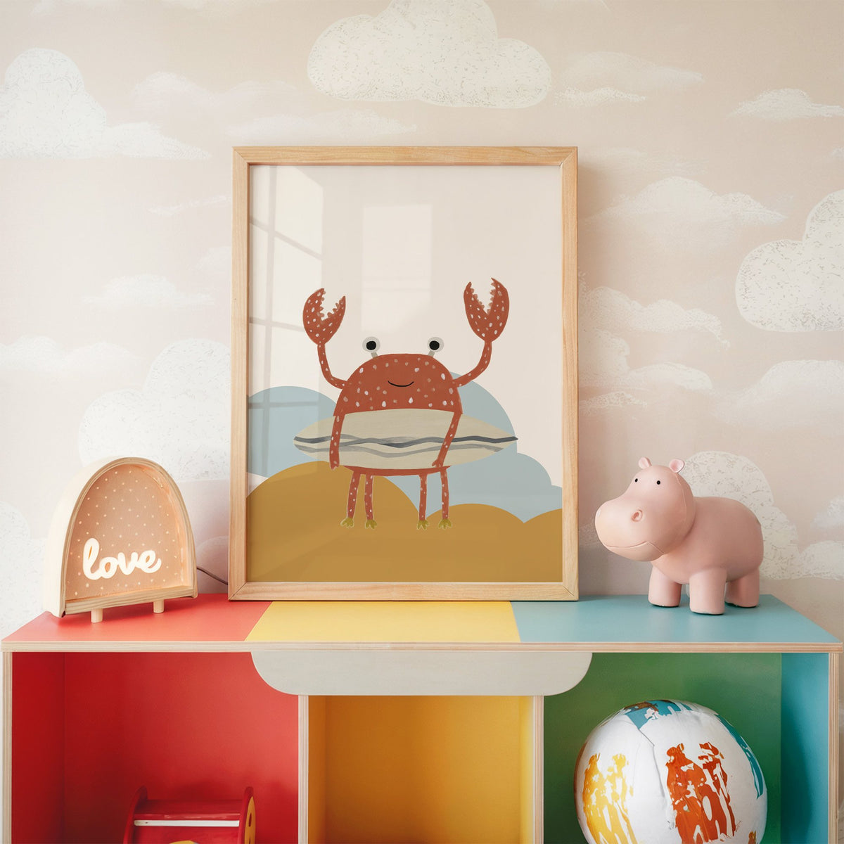 Surfing crab mustard hills nursery print in an oak frame on a rainbow toy shelf against cloud wallpaper