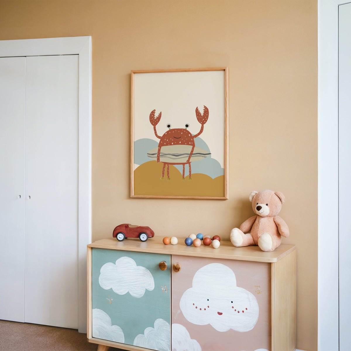Surfing crab mustard hills nursery print in an oak frame on a peach wall above a cloud-painted cabinet