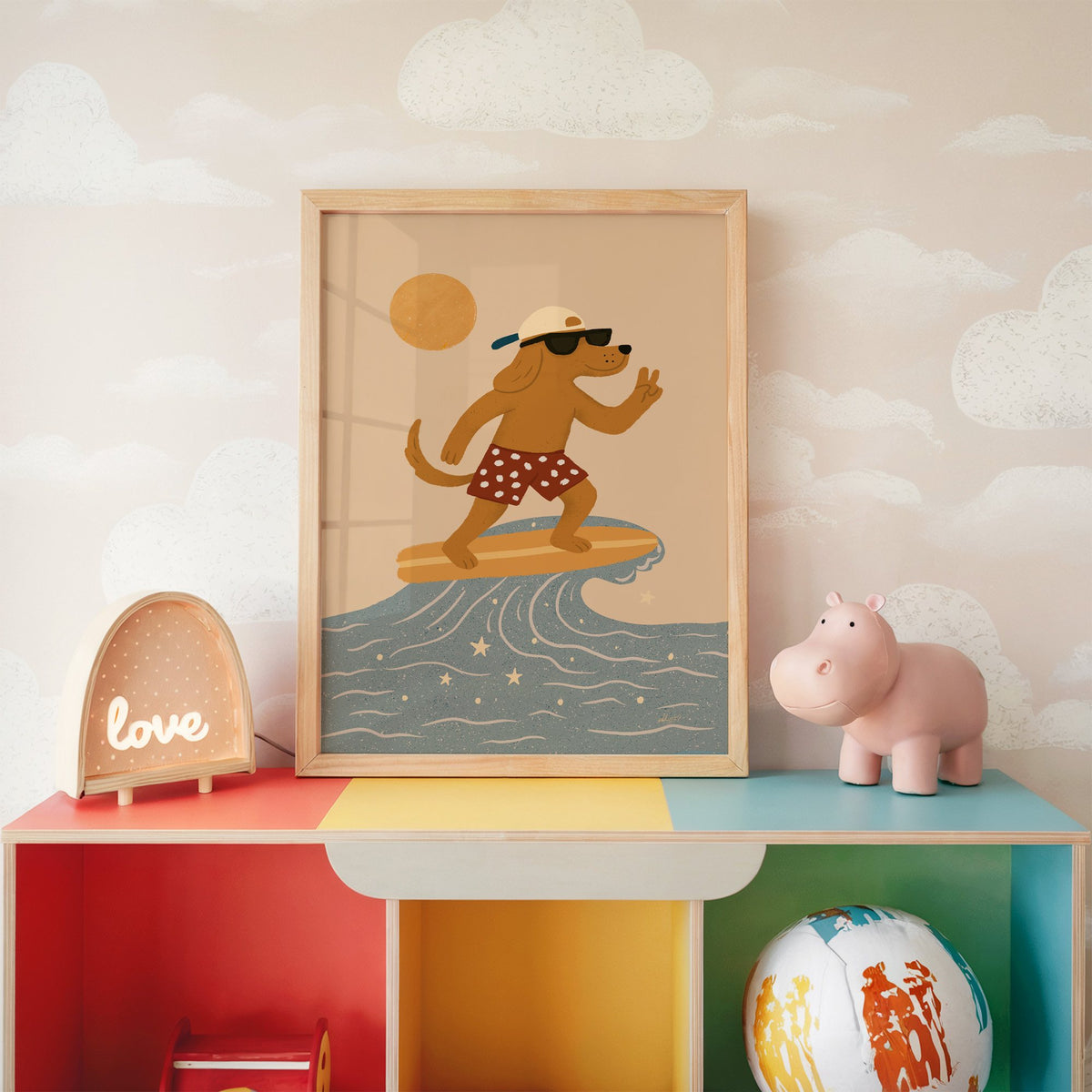 Surfing dog with peace sign nursery print in an oak frame on a rainbow toy shelf against cloud wallpaper