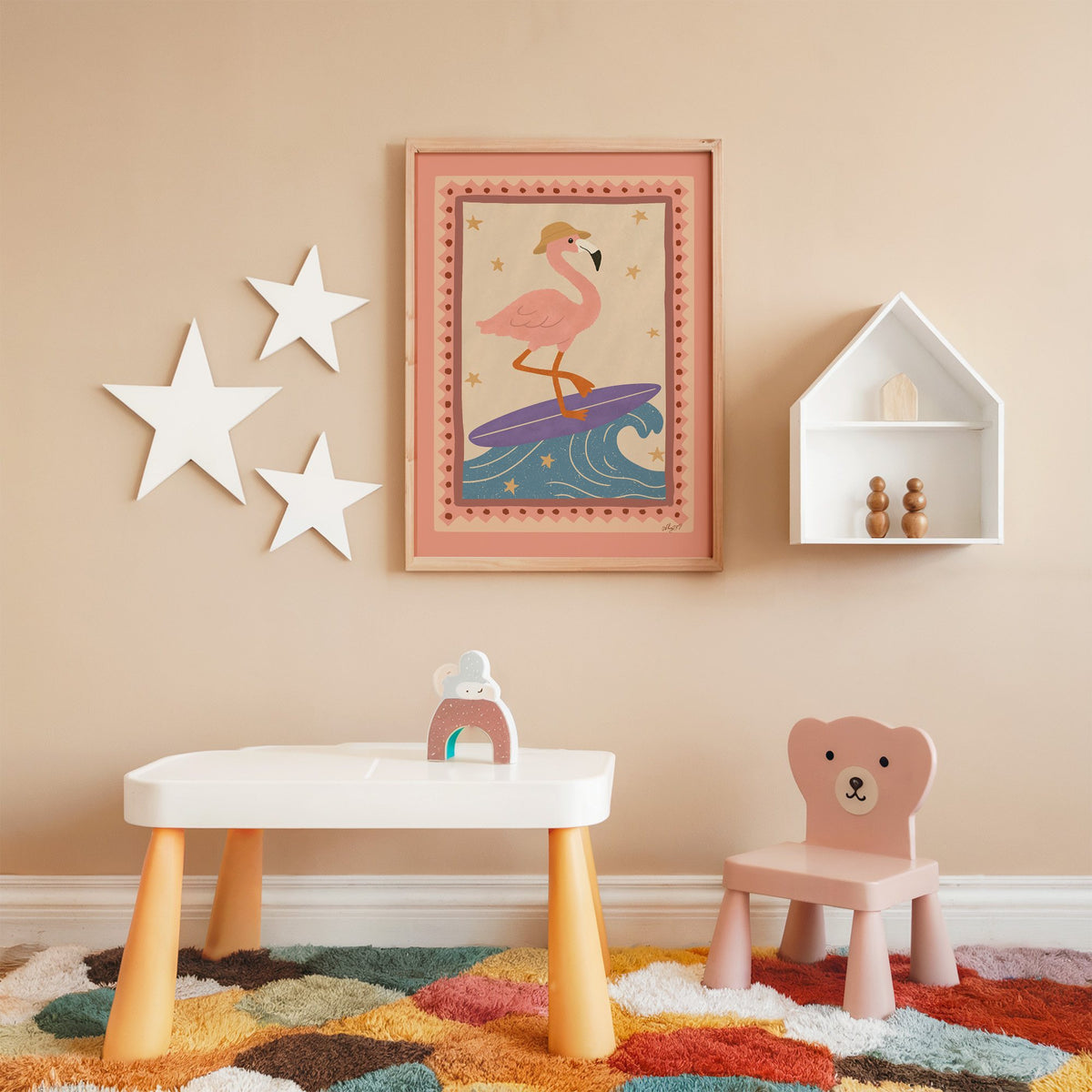 Flamingo on purple surfboard nursery print in an oak frame on a peach wall above a kids table with wall stars
