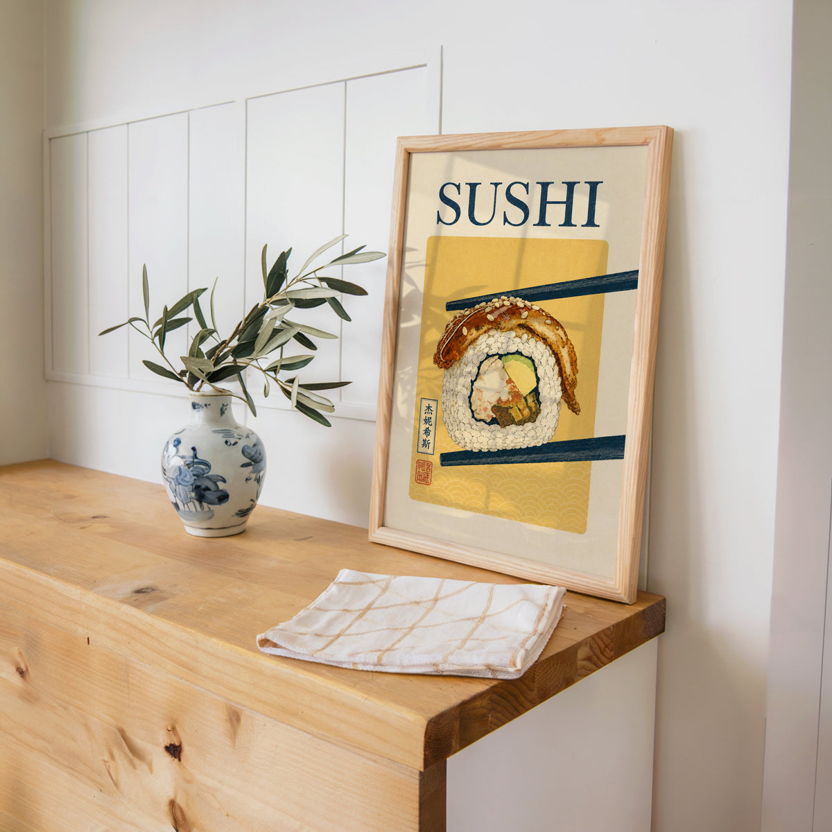 sushi roll in navy chopsticks print in a pine frame on a wooden counter beside a blue and white porcelain vase