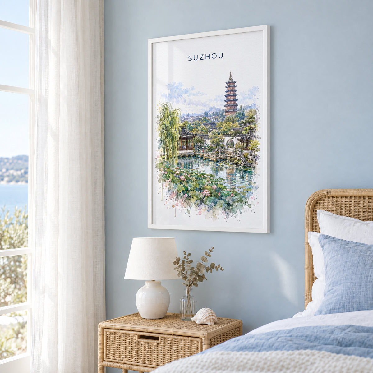 Suzhou watercolor print in a white frame on a pale blue wall beside a rattan bed in a coastal bedroom