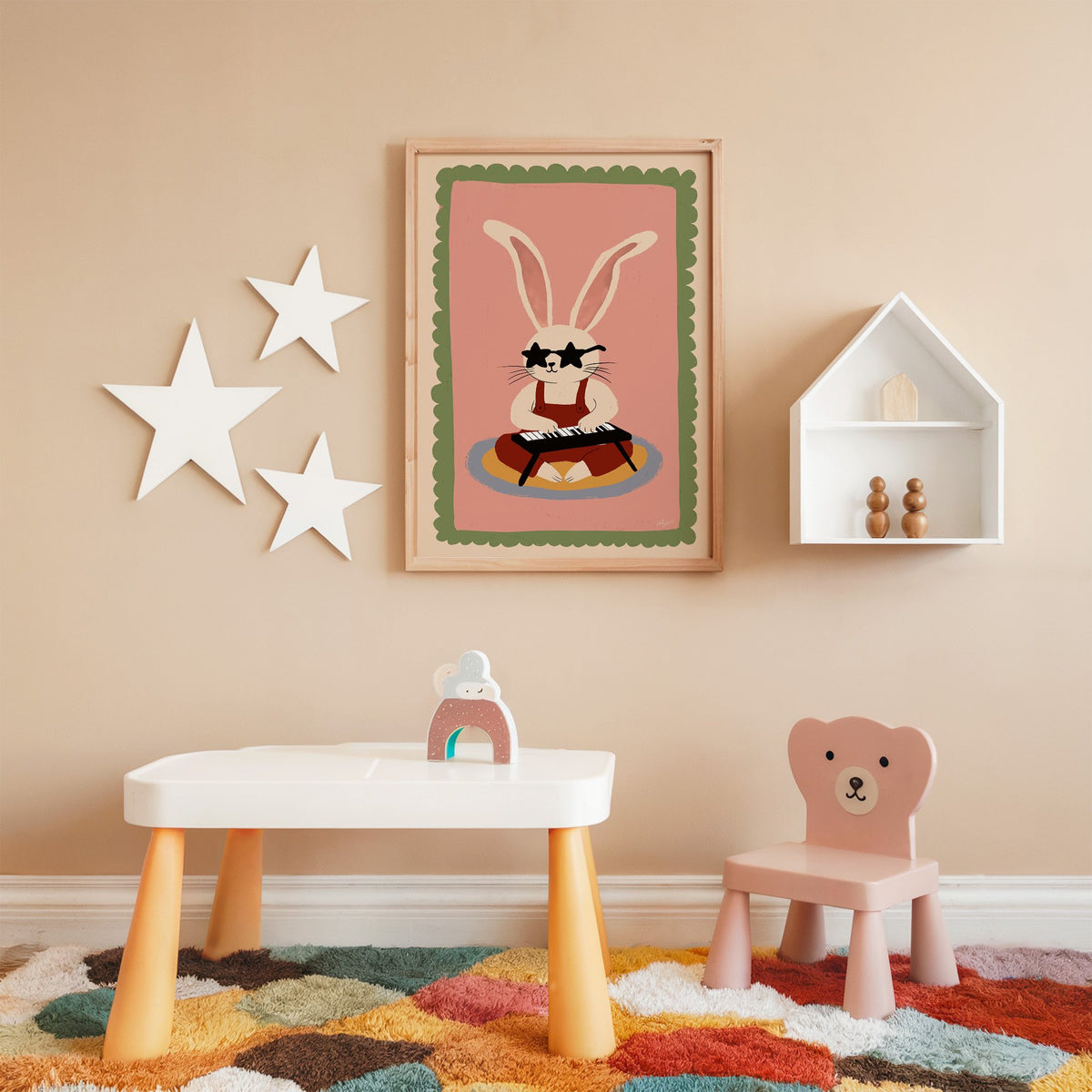 Bunny playing keyboard in star glasses nursery print in an oak frame on a peach wall above a kids table with wall stars