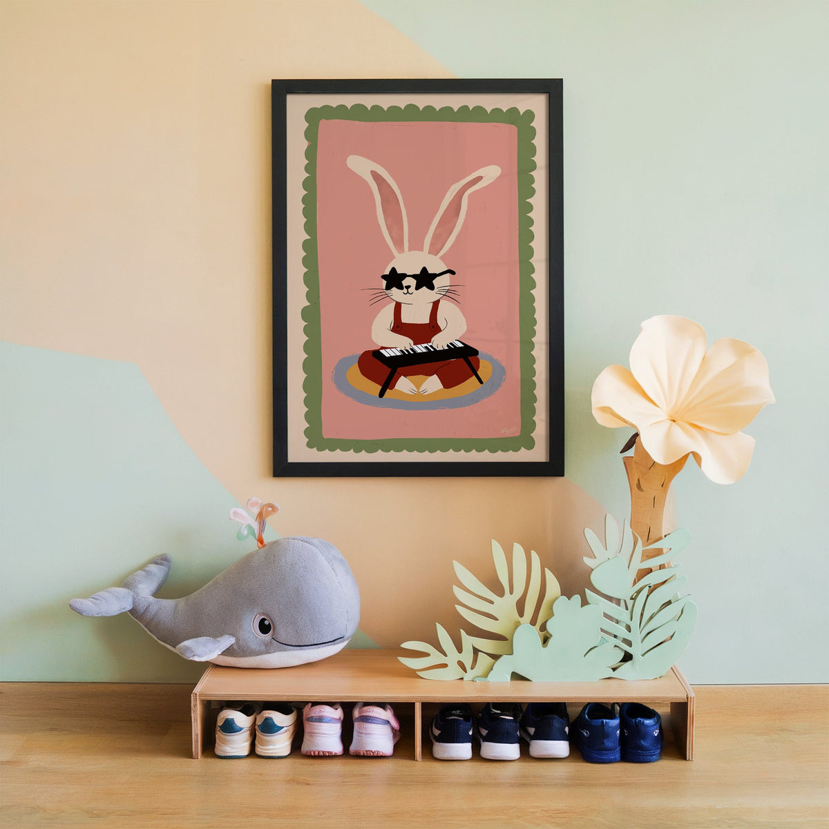 Bunny playing keyboard in star glasses nursery print in a black frame on a mint and peach wall above a whale plush