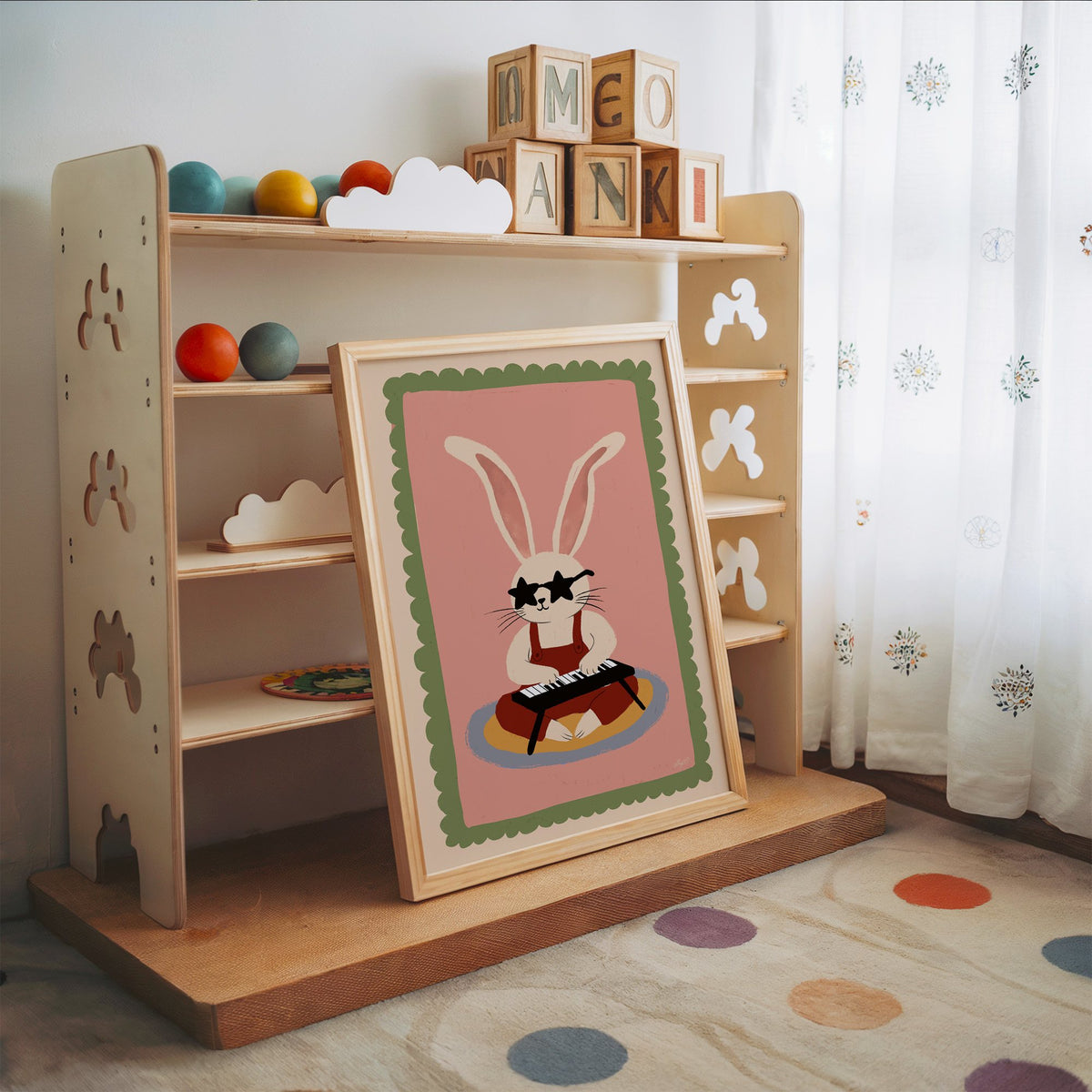 Bunny playing keyboard in star glasses nursery print in an oak frame leaning on a toy shelf with wooden letter blocks