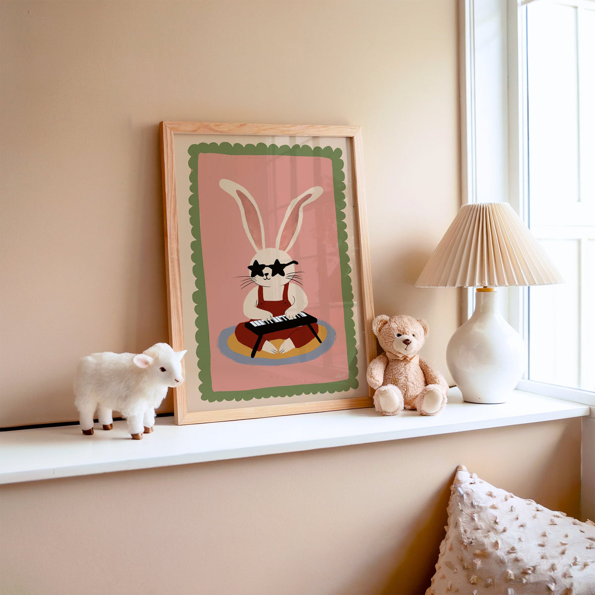 Bunny playing keyboard in star glasses nursery print in an oak frame on a window ledge with a toy lamb and teddy