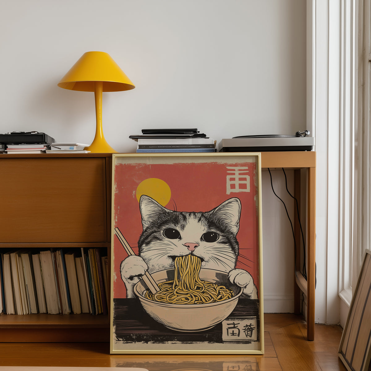 Gray tabby cat eating ramen print shown in a gold frame below a teak desk with a yellow lamp