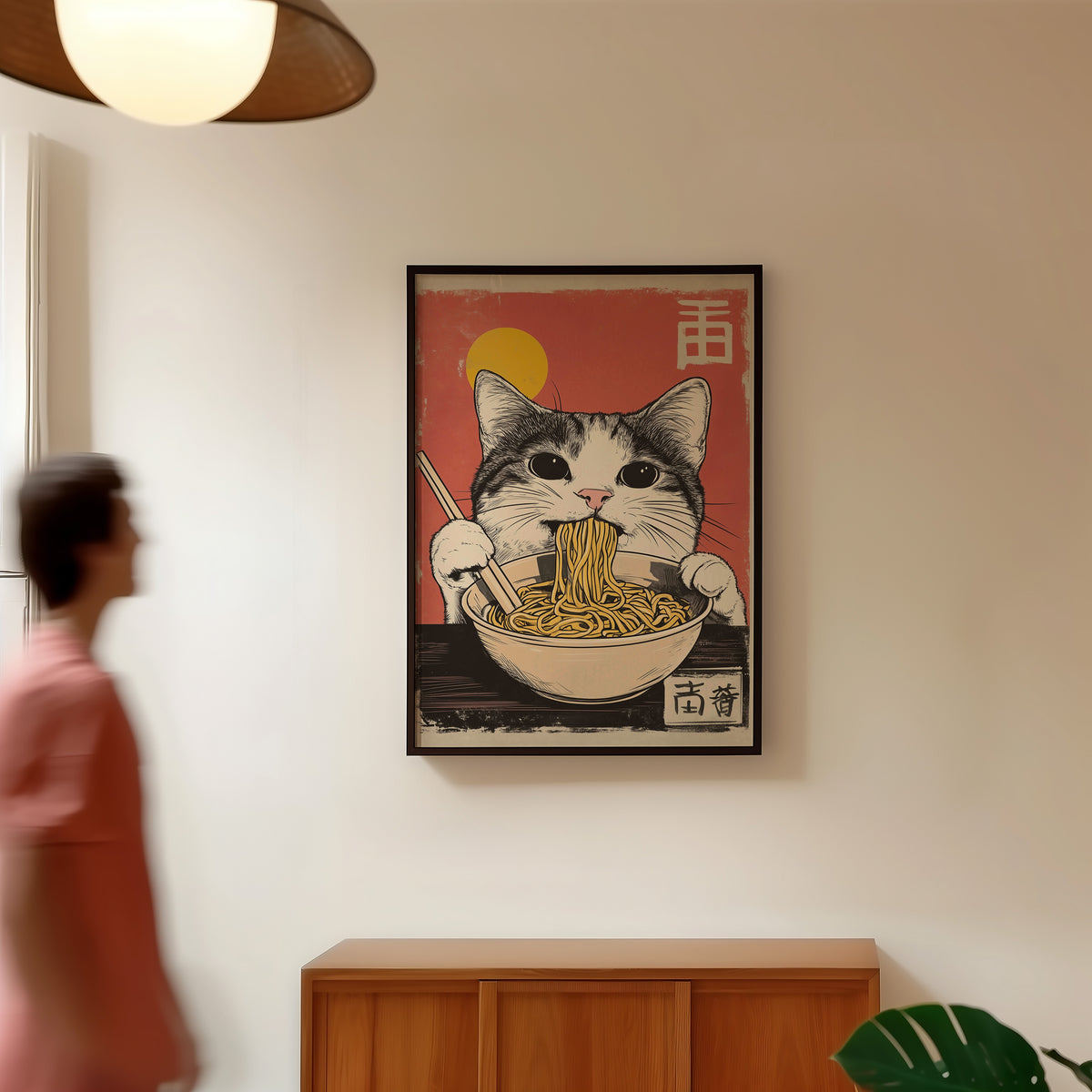Gray tabby cat eating ramen print in a black frame in a hallway under a rattan pendant
