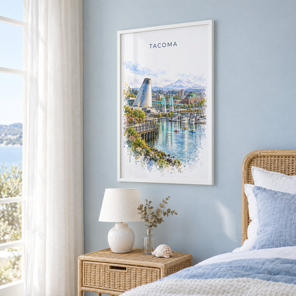 Tacoma watercolor print in a white frame on a pale blue wall beside a rattan bed in a coastal bedroom
