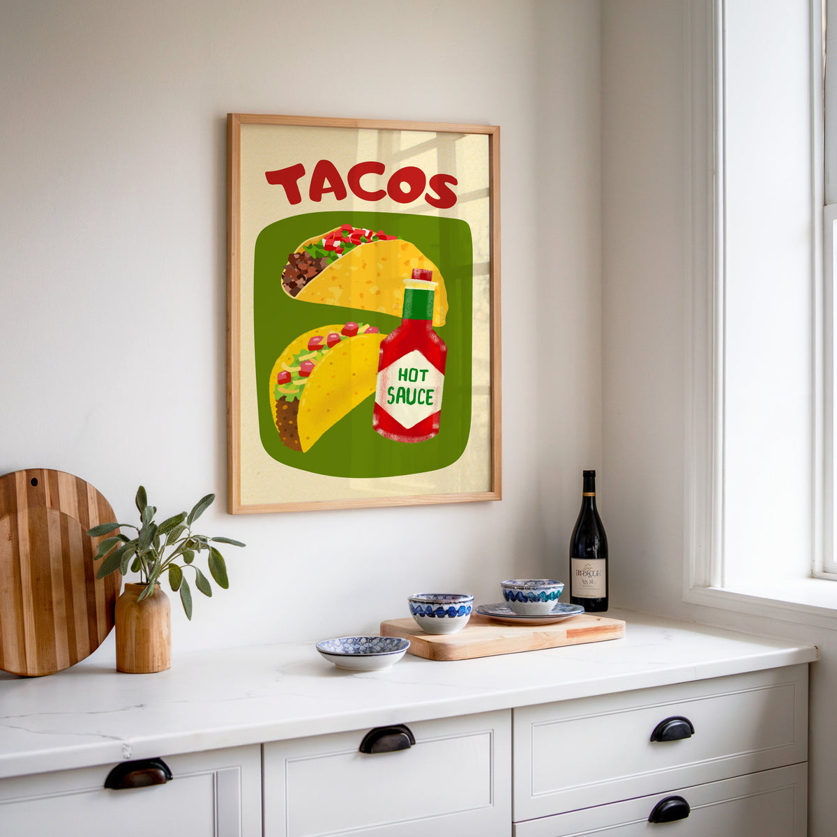 Tacos and hot sauce print in an oak frame above a white sideboard with a bottle of wine