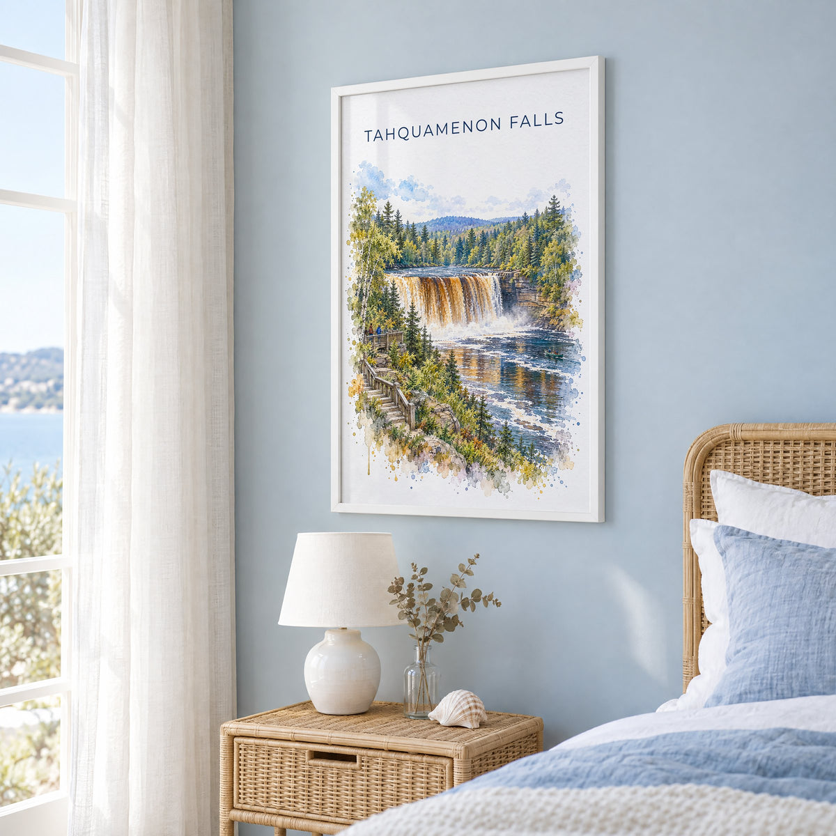 Tahquamenon Falls watercolor print in a white frame on a pale blue wall beside a rattan bed in a coastal bedroom