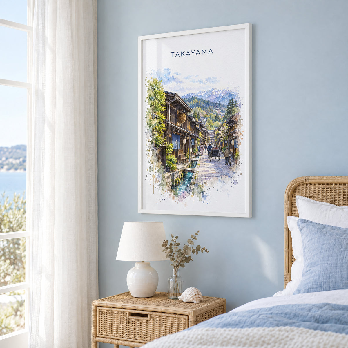 Takayama watercolor print in a white frame on a pale blue wall beside a rattan bed in a coastal bedroom