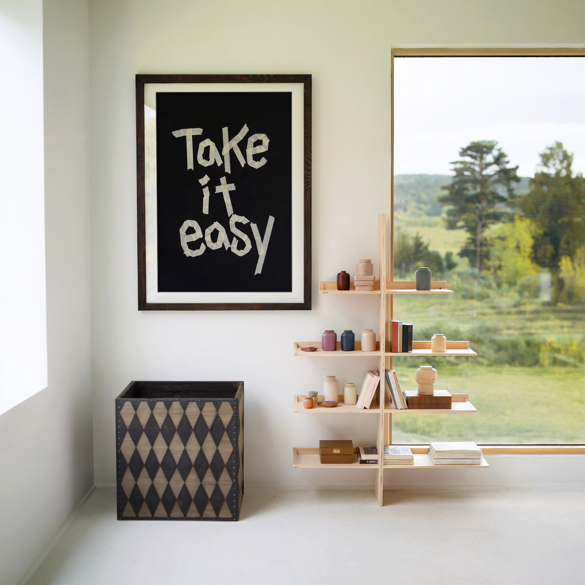 Take It Easy lowercase paper tape letters on black print in a walnut frame with a white mat beside wooden shelves and a garden window