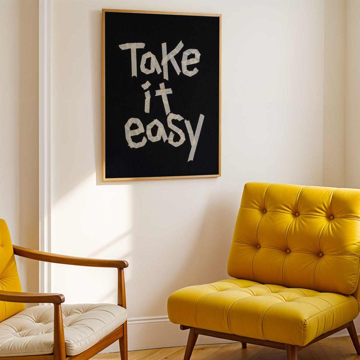 Take It Easy lowercase paper tape letters on black print shown in a gold frame above a mustard yellow tufted armchair