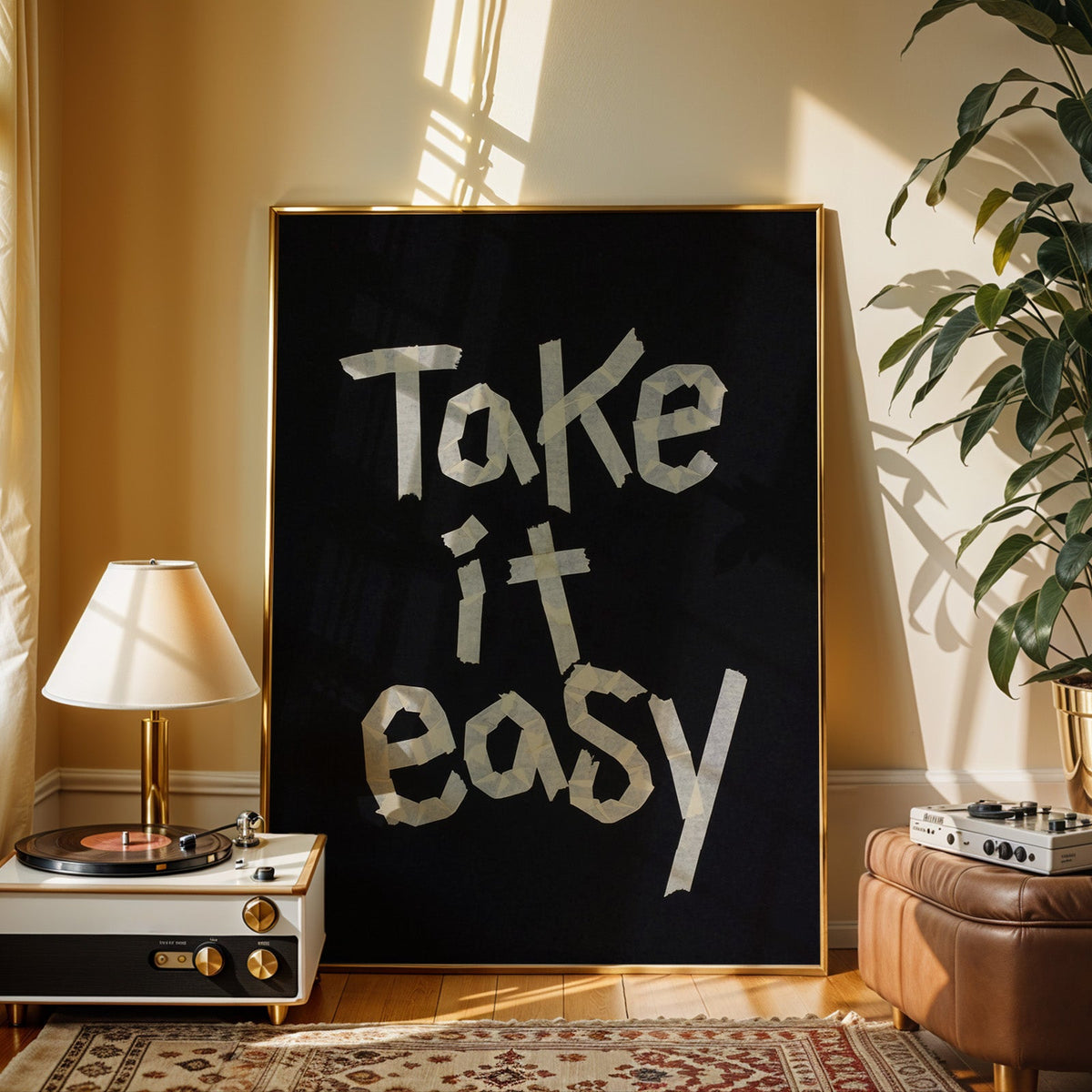 Take It Easy lowercase paper tape letters on black print shown in a gold frame beside a record player and table lamp