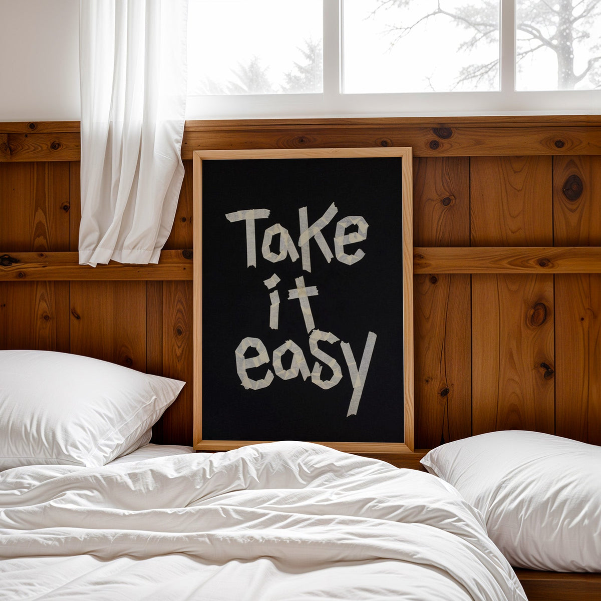 Take It Easy lowercase paper tape letters on black print in a pine frame leaning on a wood headboard over white bedding