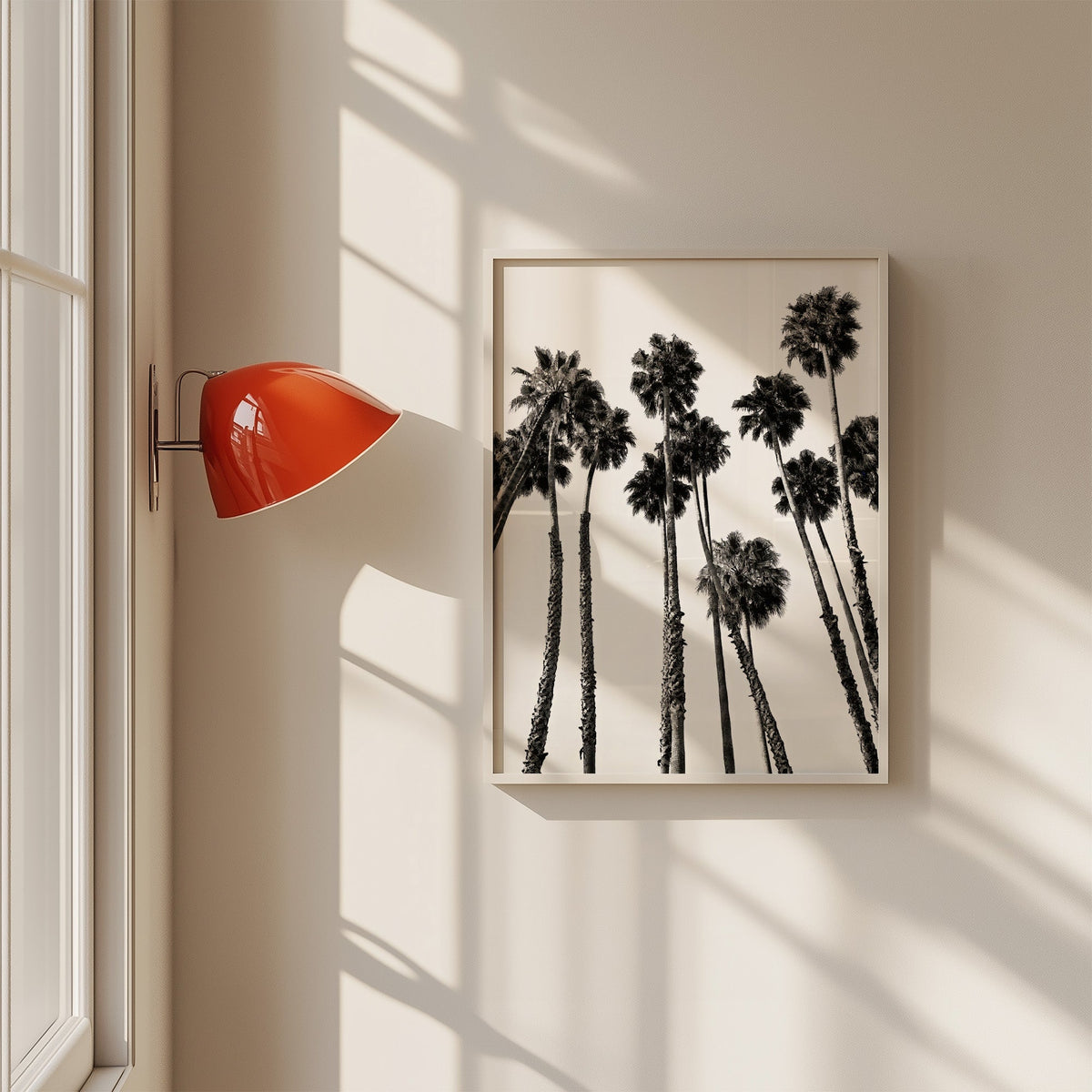 Dense fan palm grove seen from below print in a white frame on a sunlit wall beside a red sconce