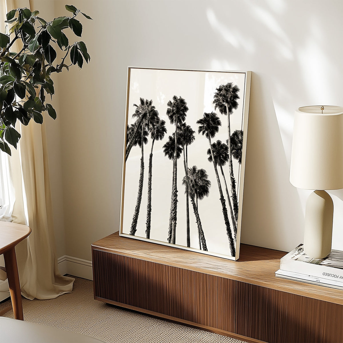Dense fan palm grove seen from below print in a white frame on a walnut sideboard beside a ceramic lamp