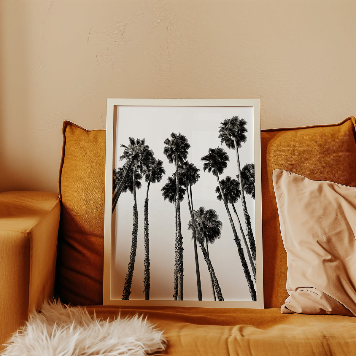 Dense fan palm grove seen from below print in a white frame leaning on a mustard velvet sofa