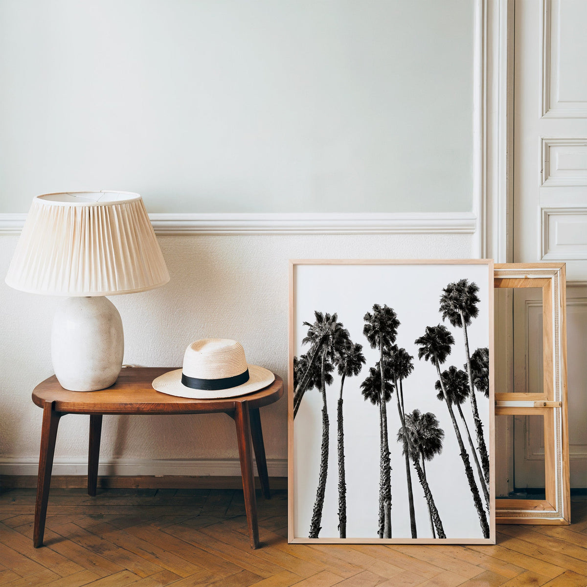 Dense fan palm grove seen from below print in a pine frame on a wood floor beside a lamp and straw hat