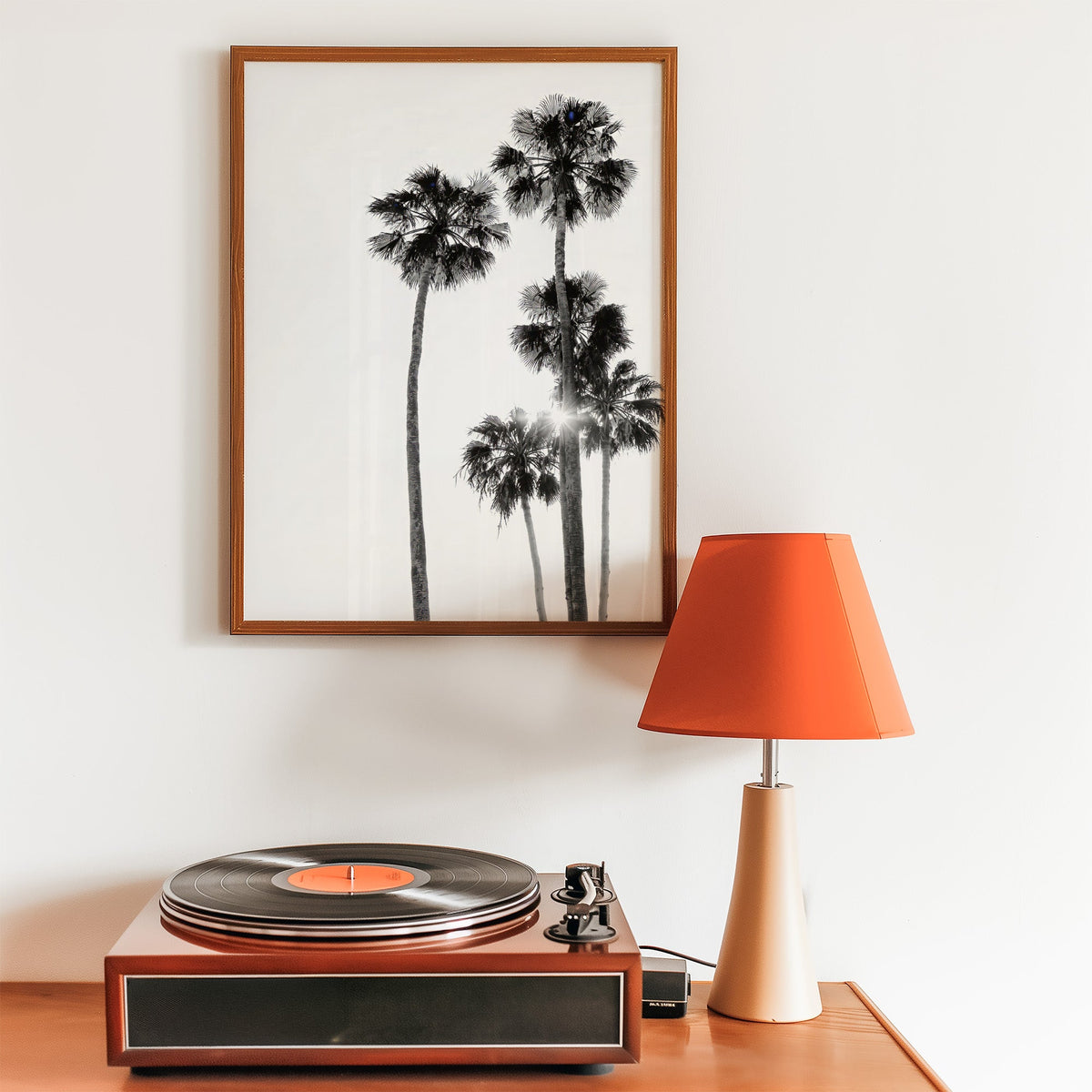 Five tall fan palms with sun flare print in a walnut frame above a record player and orange lamp