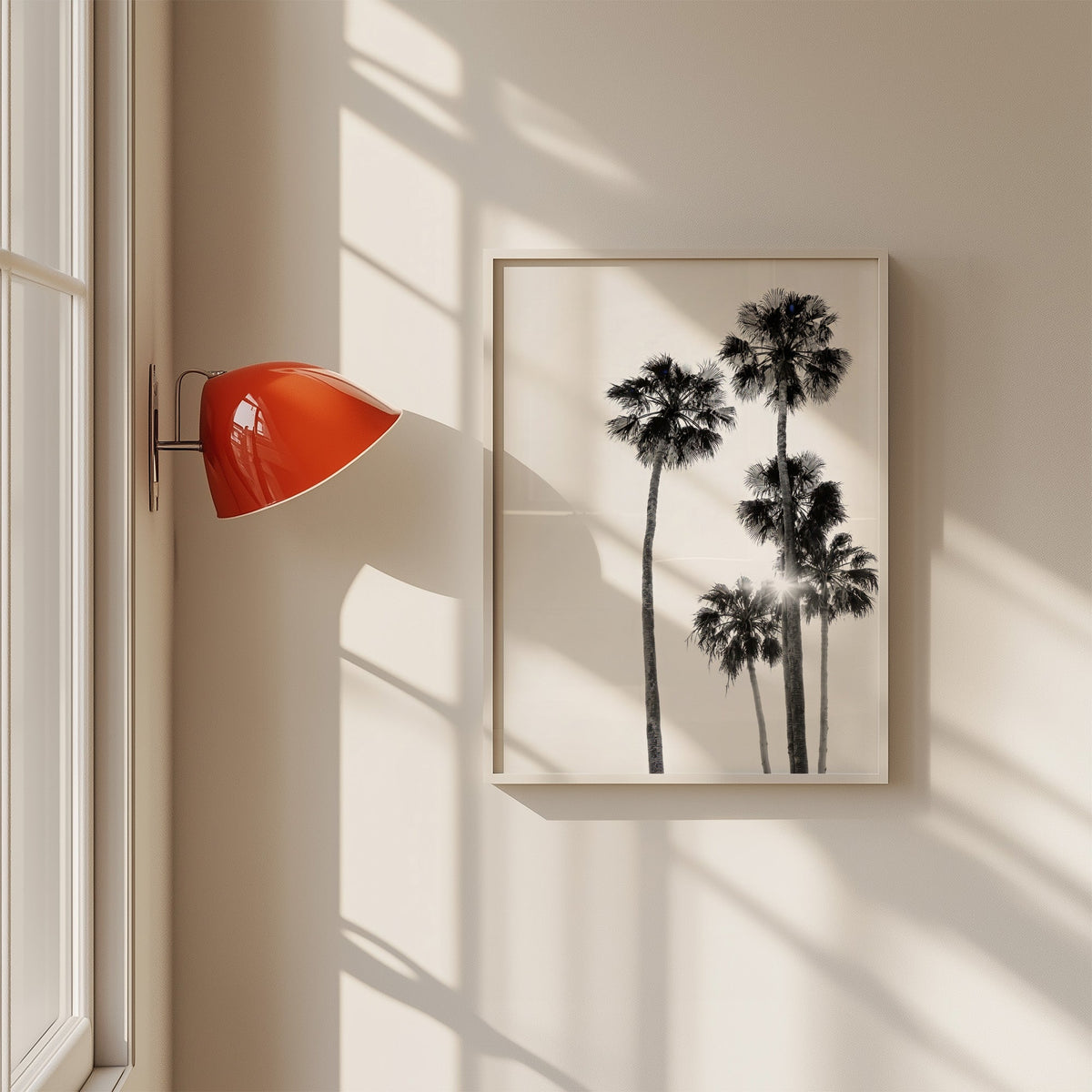 Five tall fan palms with sun flare print in a white frame on a sunlit wall beside a red sconce