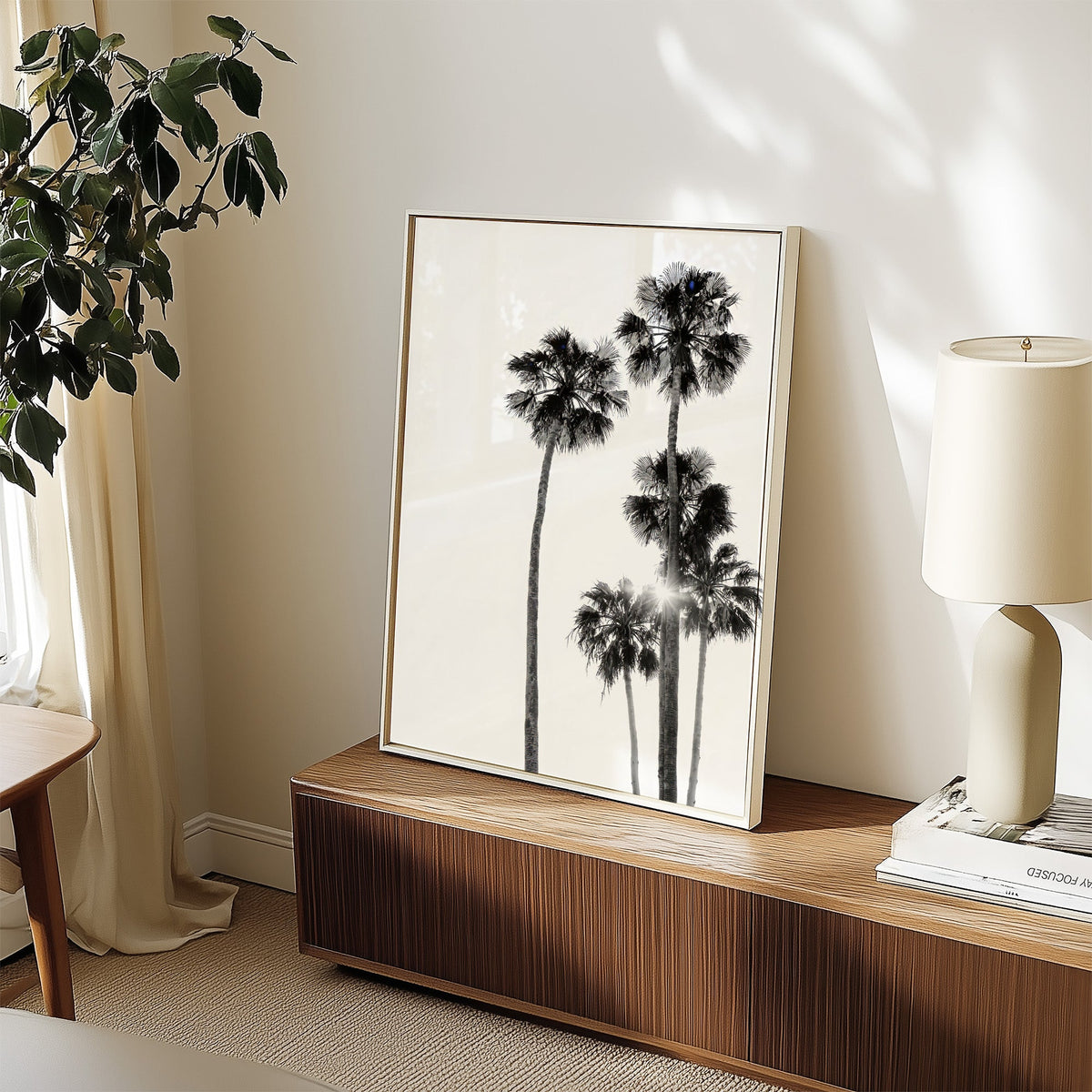 Five tall fan palms with sun flare print in a white frame on a walnut sideboard beside a ceramic lamp