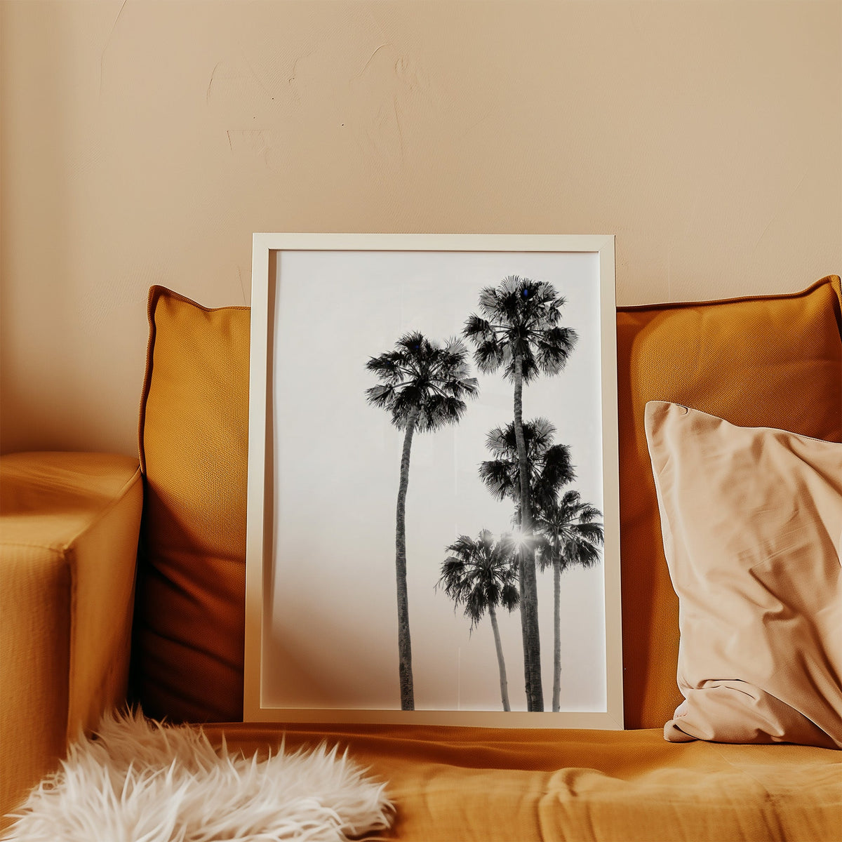 Five tall fan palms with sun flare print in a white frame leaning on a mustard velvet sofa
