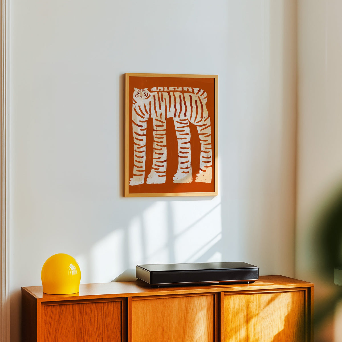 Long-legged tiger print in a light oak frame above a teak sideboard with a yellow lamp