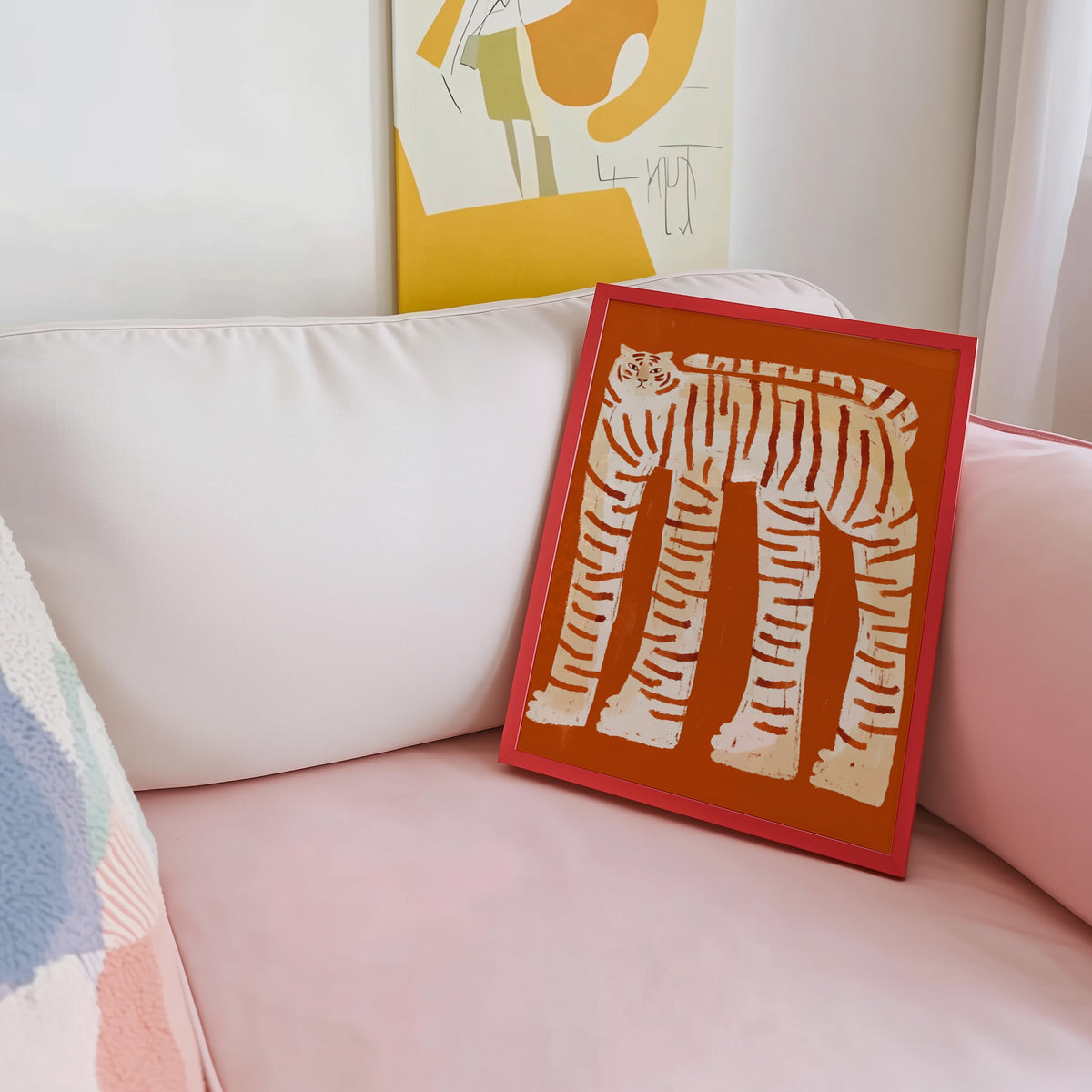 Burnt orange tiger print shown in a red frame leaning on a blush pink sofa
