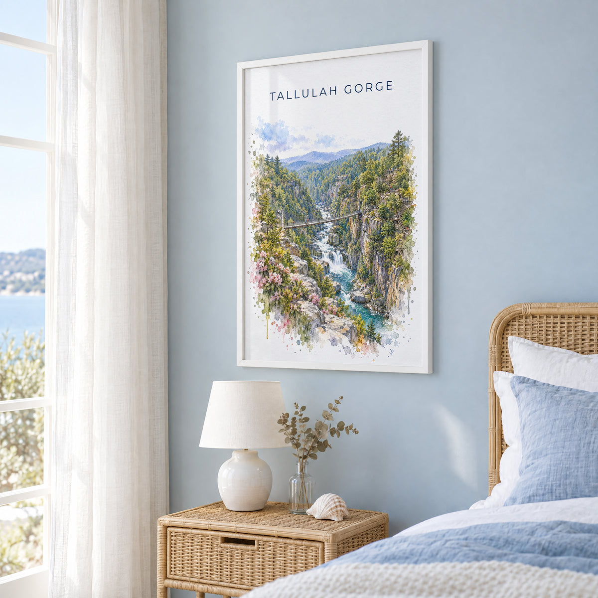 Tallulah Gorge watercolor print in a white frame on a pale blue wall beside a rattan bed in a coastal bedroom
