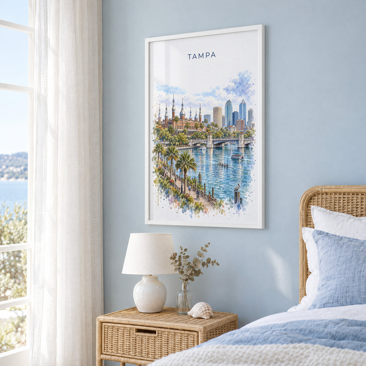Tampa watercolor print in a white frame on a pale blue wall beside a rattan bed in a coastal bedroom