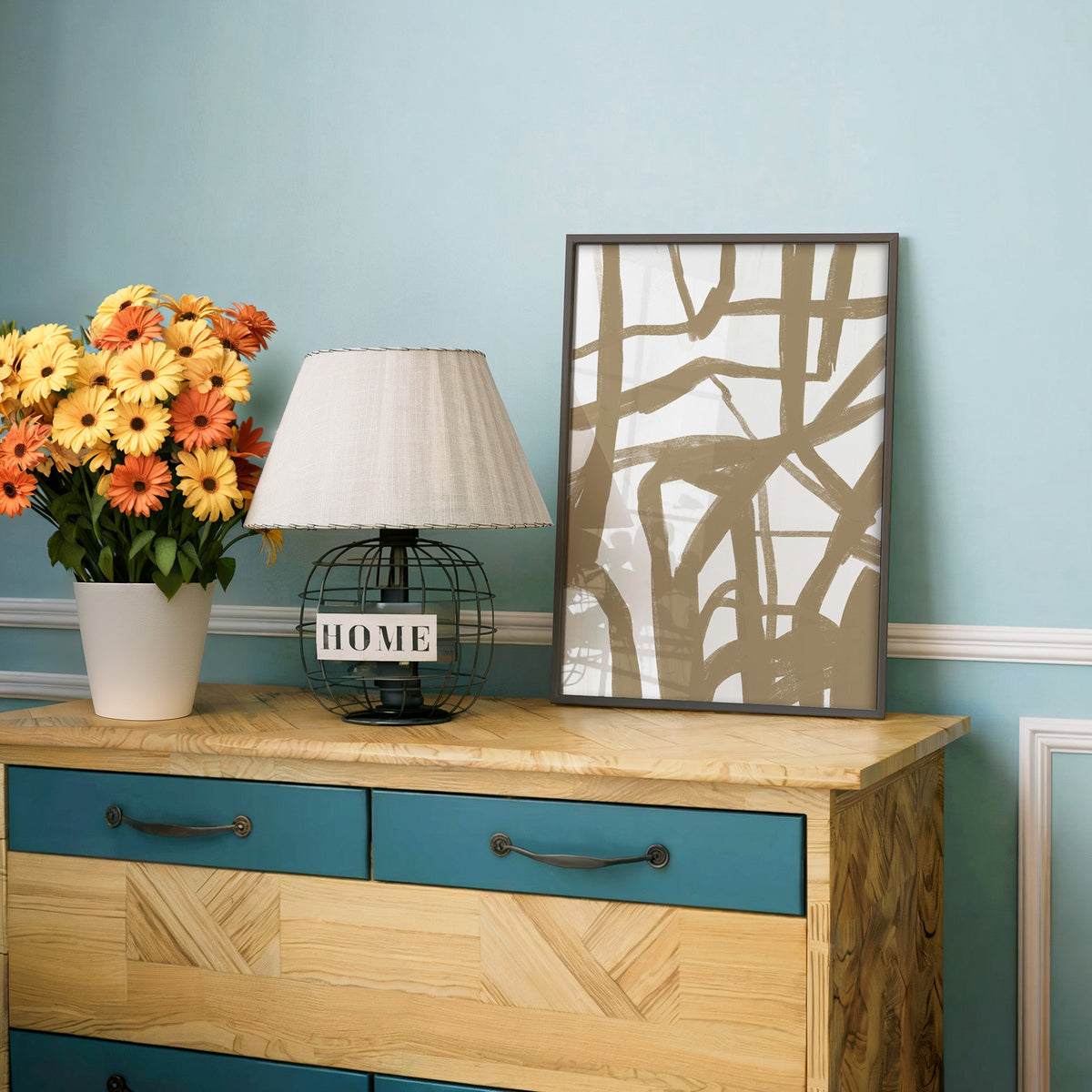 Tan crisscross brushstroke lattice print in a charcoal frame on a teal dresser beside orange and yellow daisies