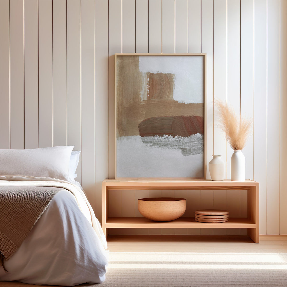 Tan and rust brush blocks on white boho print in a light oak frame on a wood bench by a bed with pampas grass