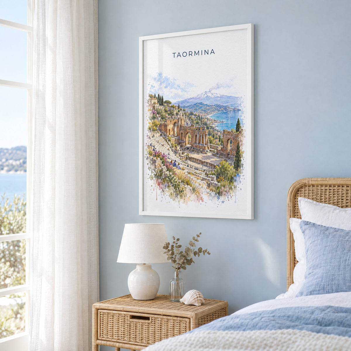 Taormina watercolor print in a white frame on a pale blue wall beside a rattan bed in a coastal bedroom
