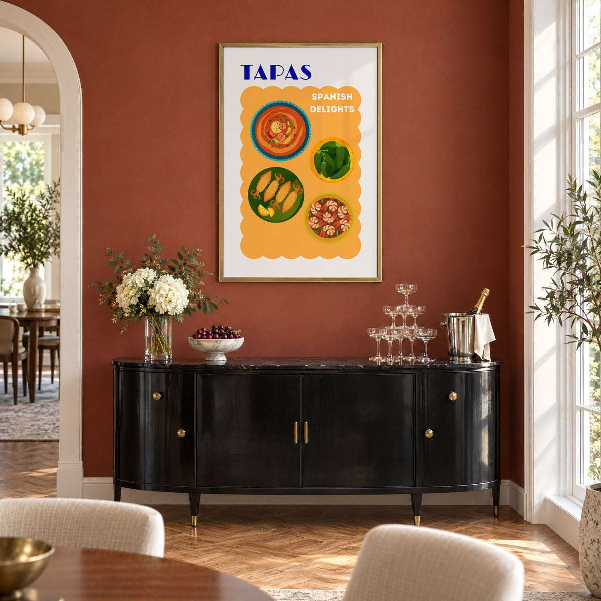 TAPAS Spanish Delights four plates print in a brass frame on a terracotta wall above a black buffet with a champagne tower