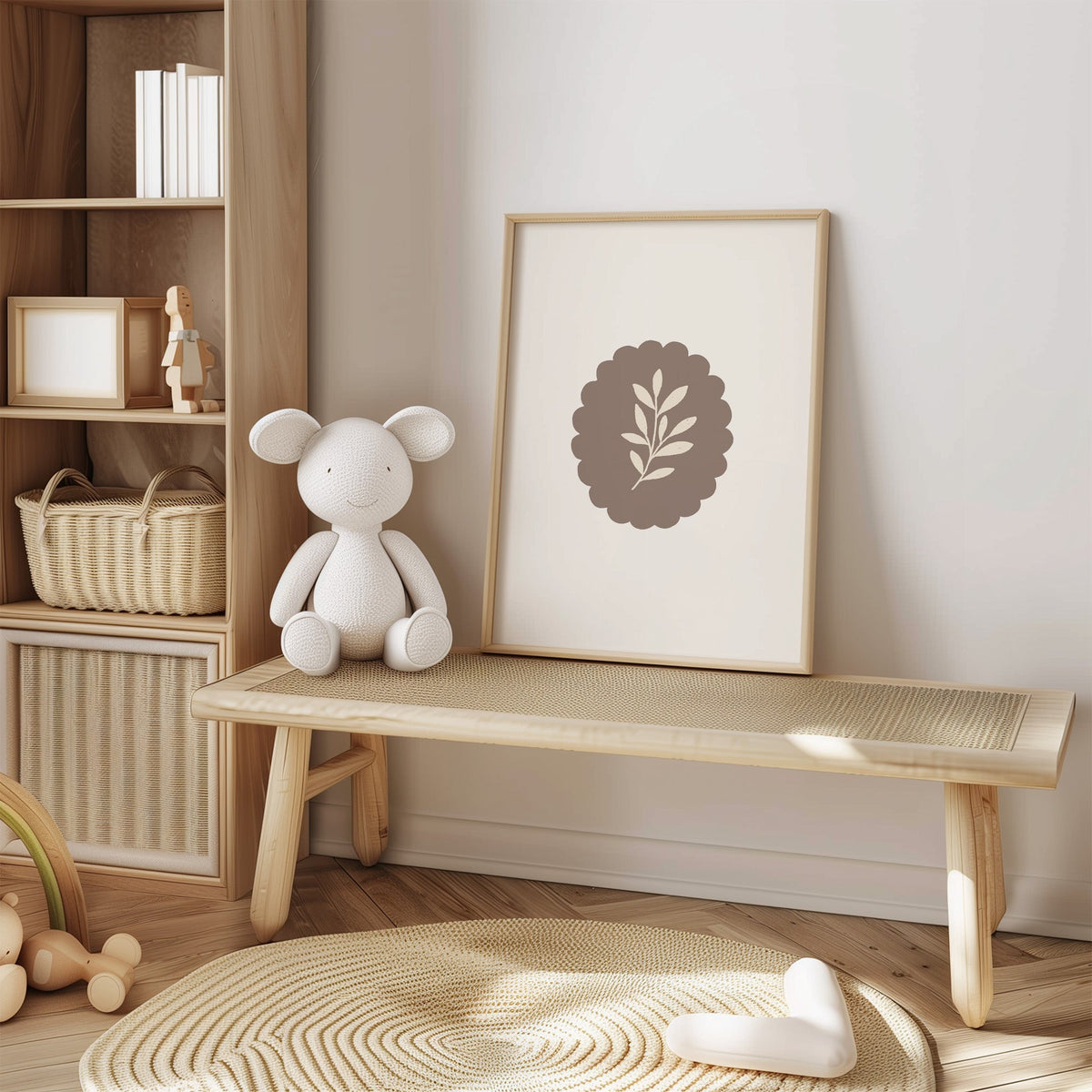 Cream leaf sprig on taupe scalloped oval nursery print in an oak frame on a cane bench beside a white knit plush