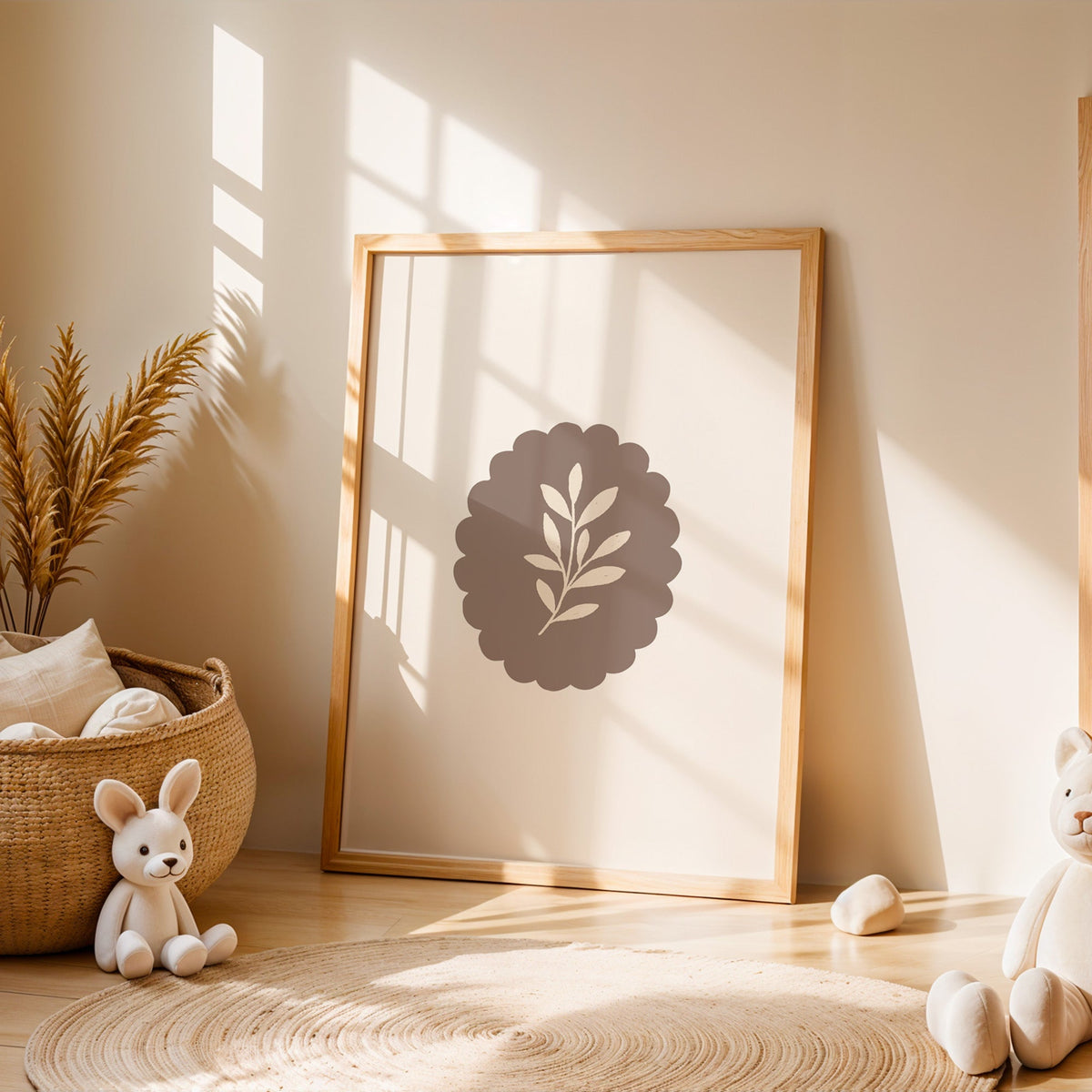 Cream leaf sprig on taupe scalloped oval nursery print in an oak frame leaning on a sunlit floor by a woven basket