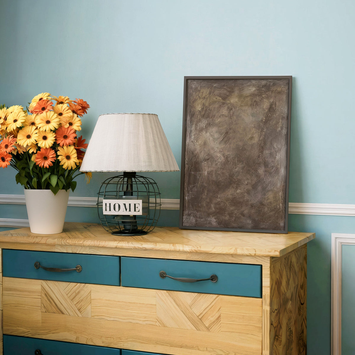 Taupe Venetian plaster textured abstract print in a charcoal frame on a teal dresser beside orange and yellow daisies