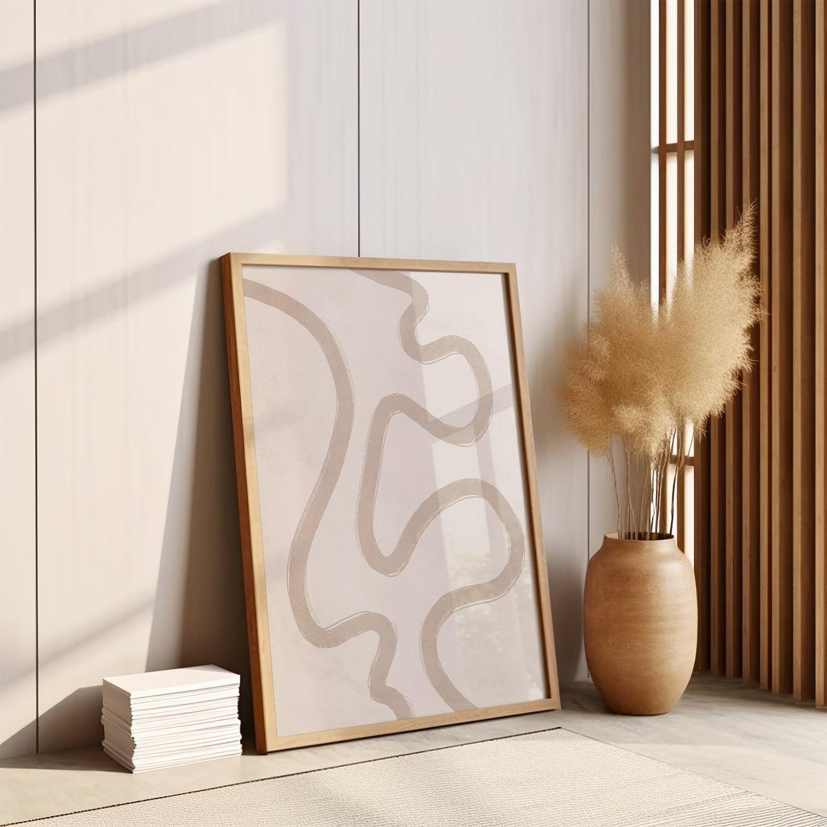 Taupe squiggle brushstroke neutral boho print in an oak frame leaning on the floor by pampas grass and a wood slat screen