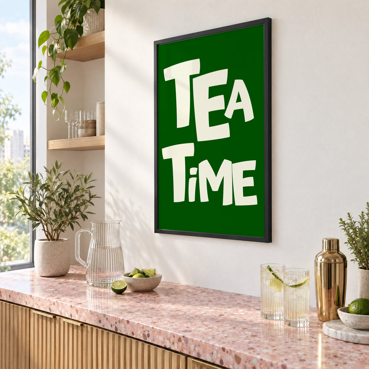 TEA TiME green typography print in a black frame above a pink terrazzo cocktail counter with limes, seen at an angle