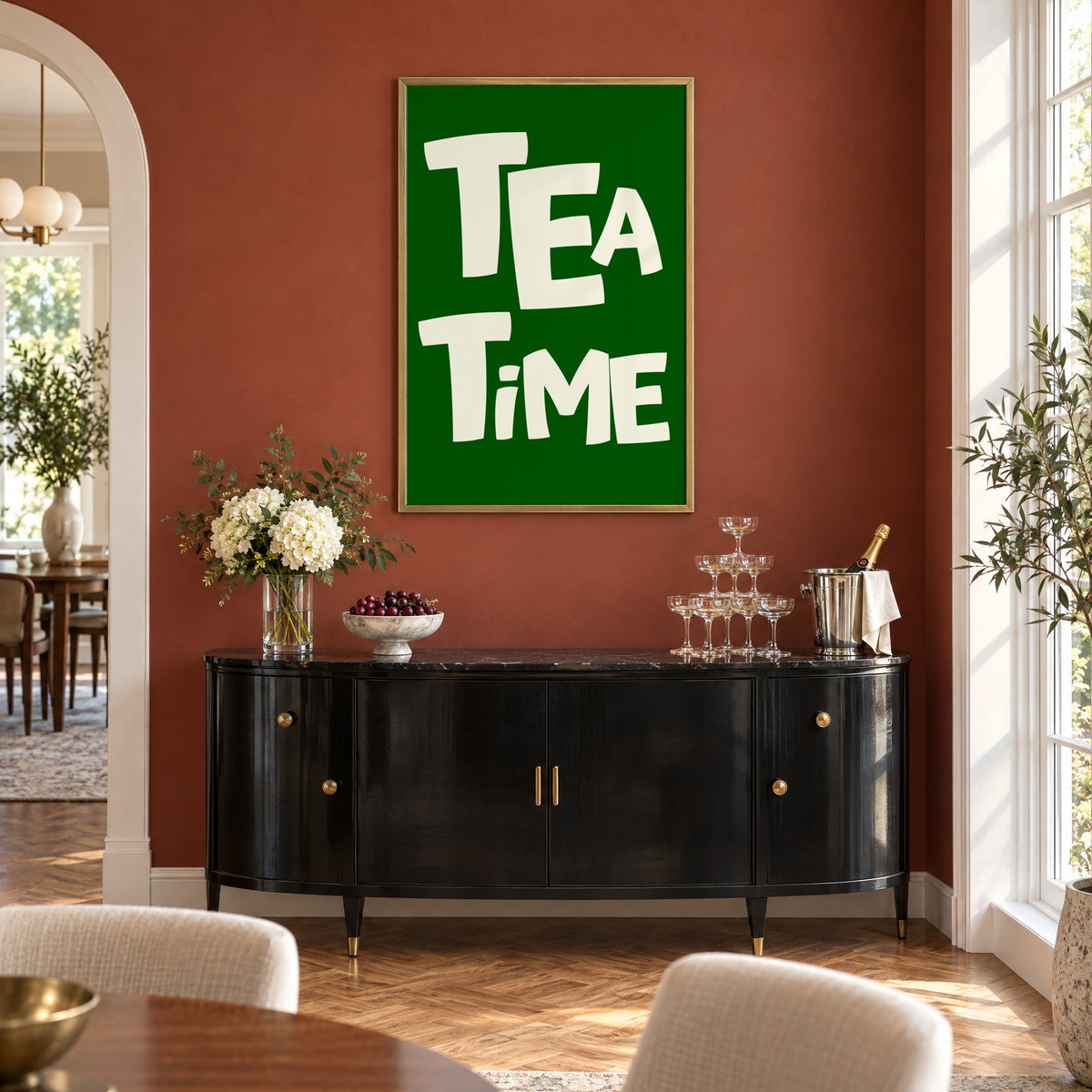 TEA TiME green typography print in a brass frame on a terracotta wall above a black buffet with a champagne tower
