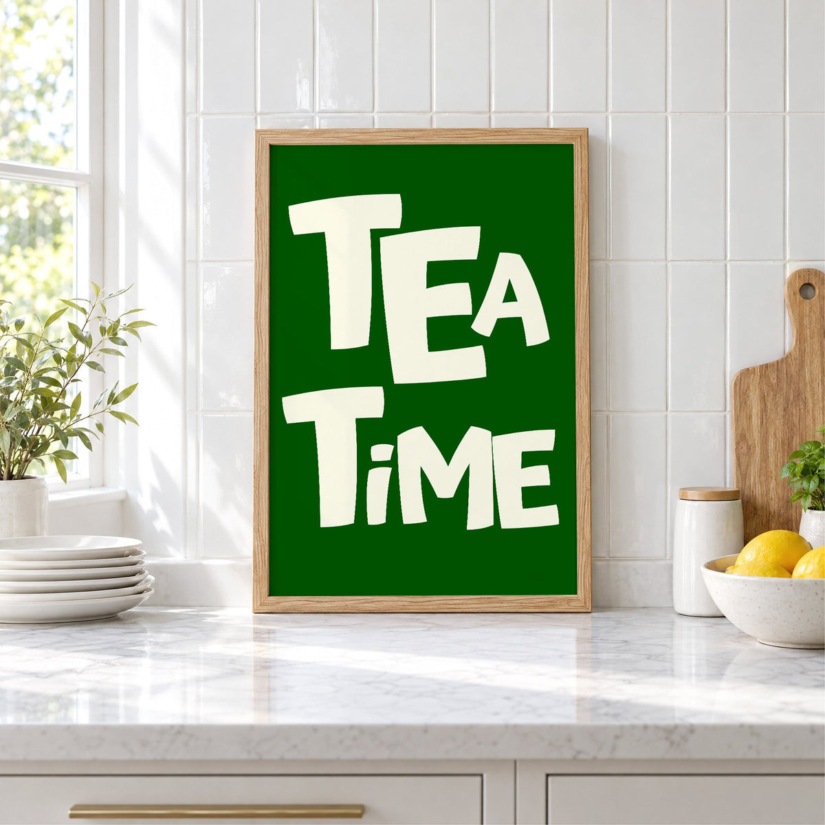 TEA TiME green typography print in an oak frame leaning on a marble counter by white tiles and lemons