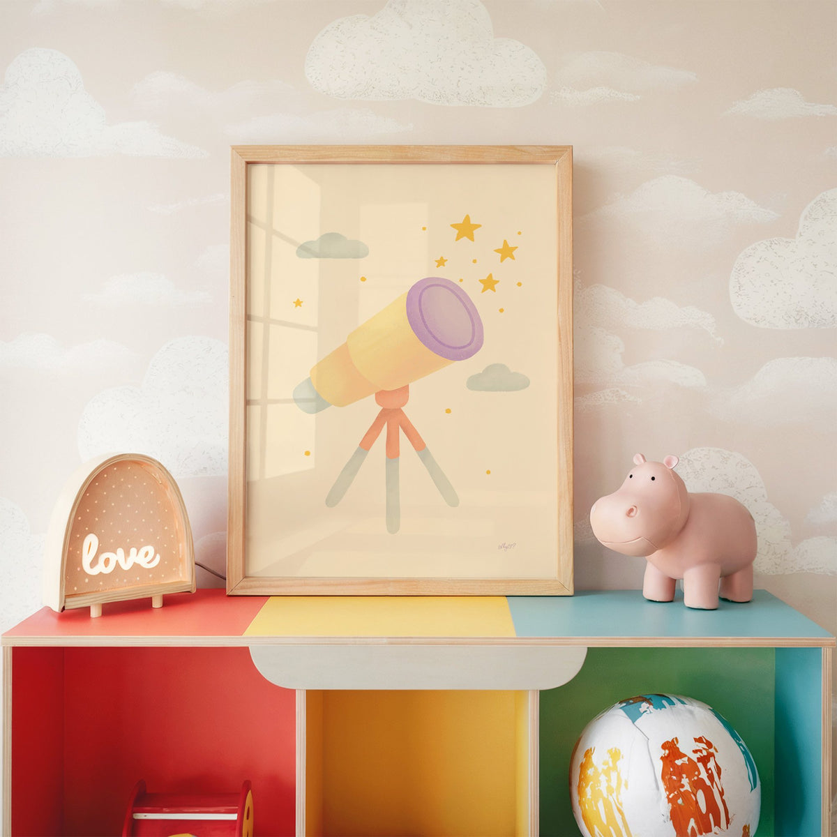 Pastel telescope and gold stars nursery print in an oak frame on a rainbow toy shelf against cloud wallpaper
