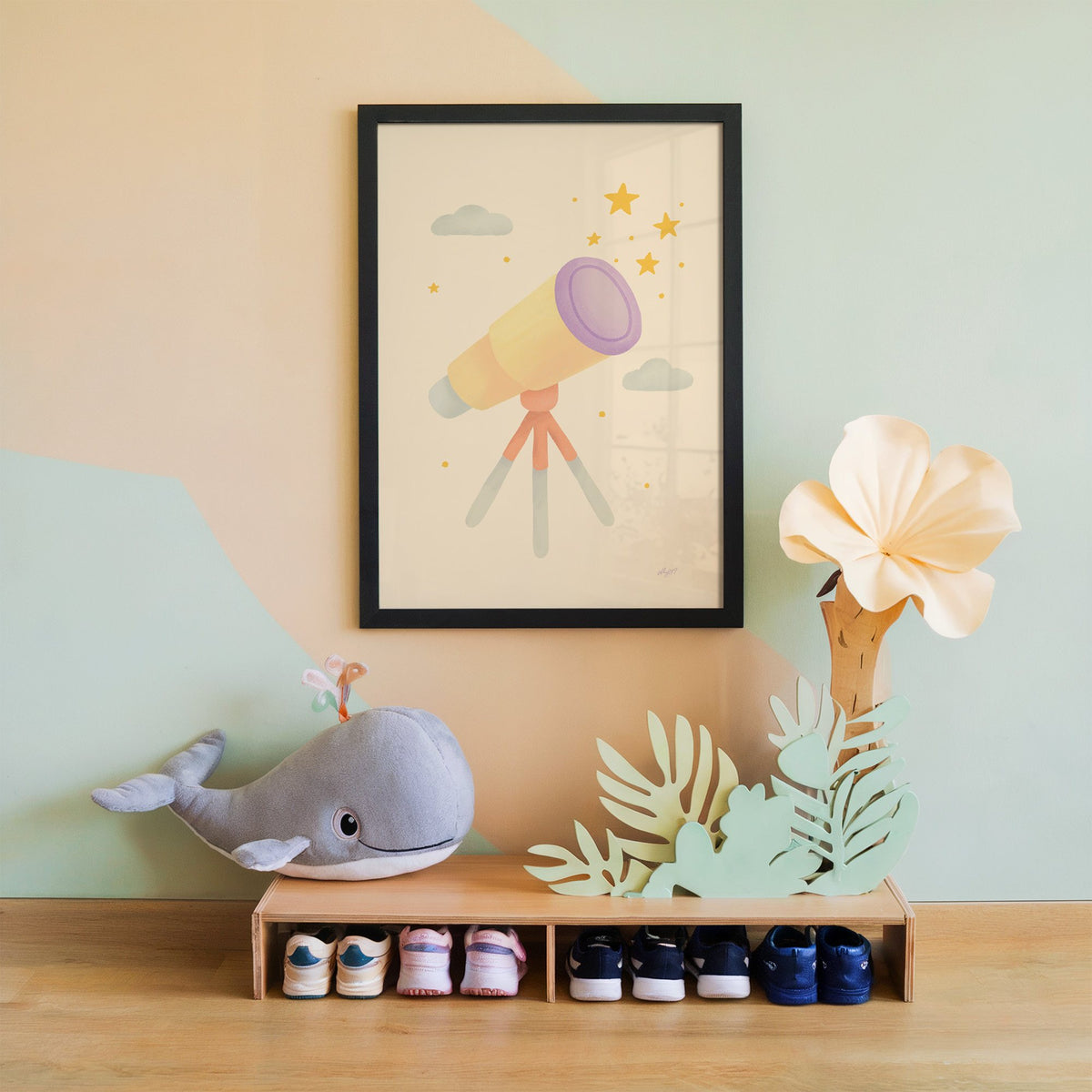 Pastel telescope and gold stars nursery print in a black frame on a mint and peach wall above a whale plush