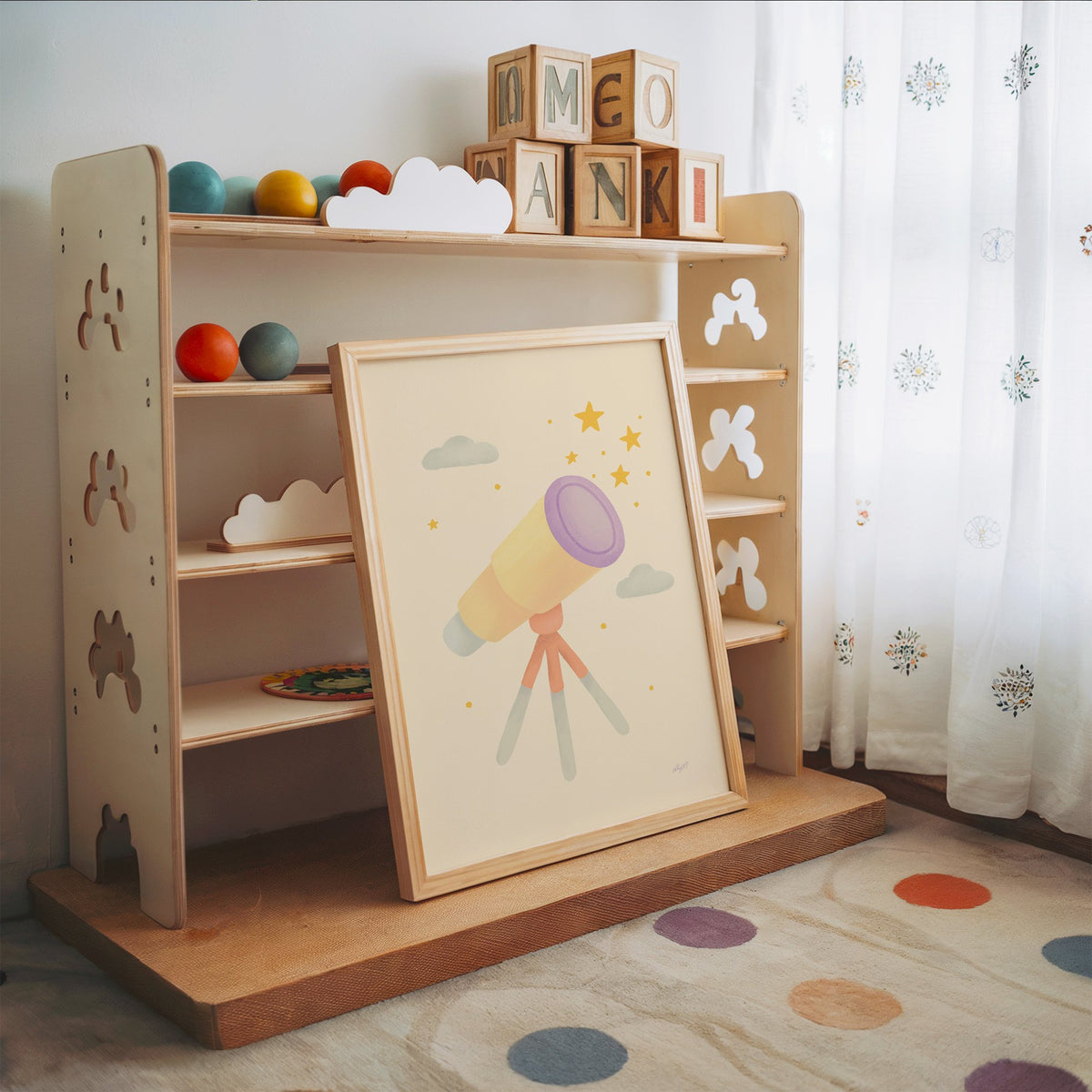 Pastel telescope and gold stars nursery print in an oak frame leaning on a toy shelf with wooden letter blocks