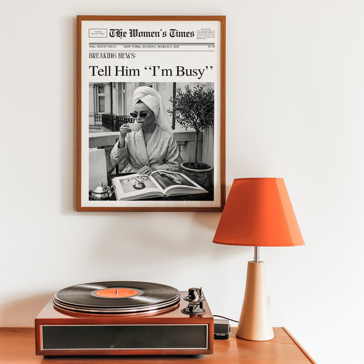 Woman with tea and photo book on balcony newspaper print in a walnut frame above a record player and orange lamp