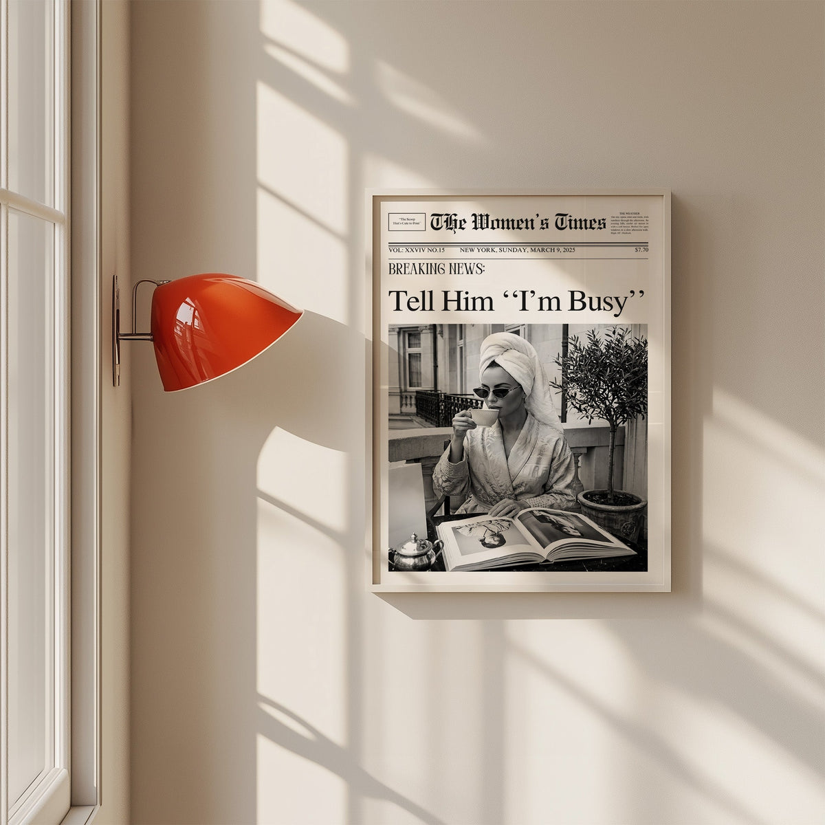 Woman with tea and photo book on balcony newspaper print in a white frame on a sunlit wall beside a red sconce