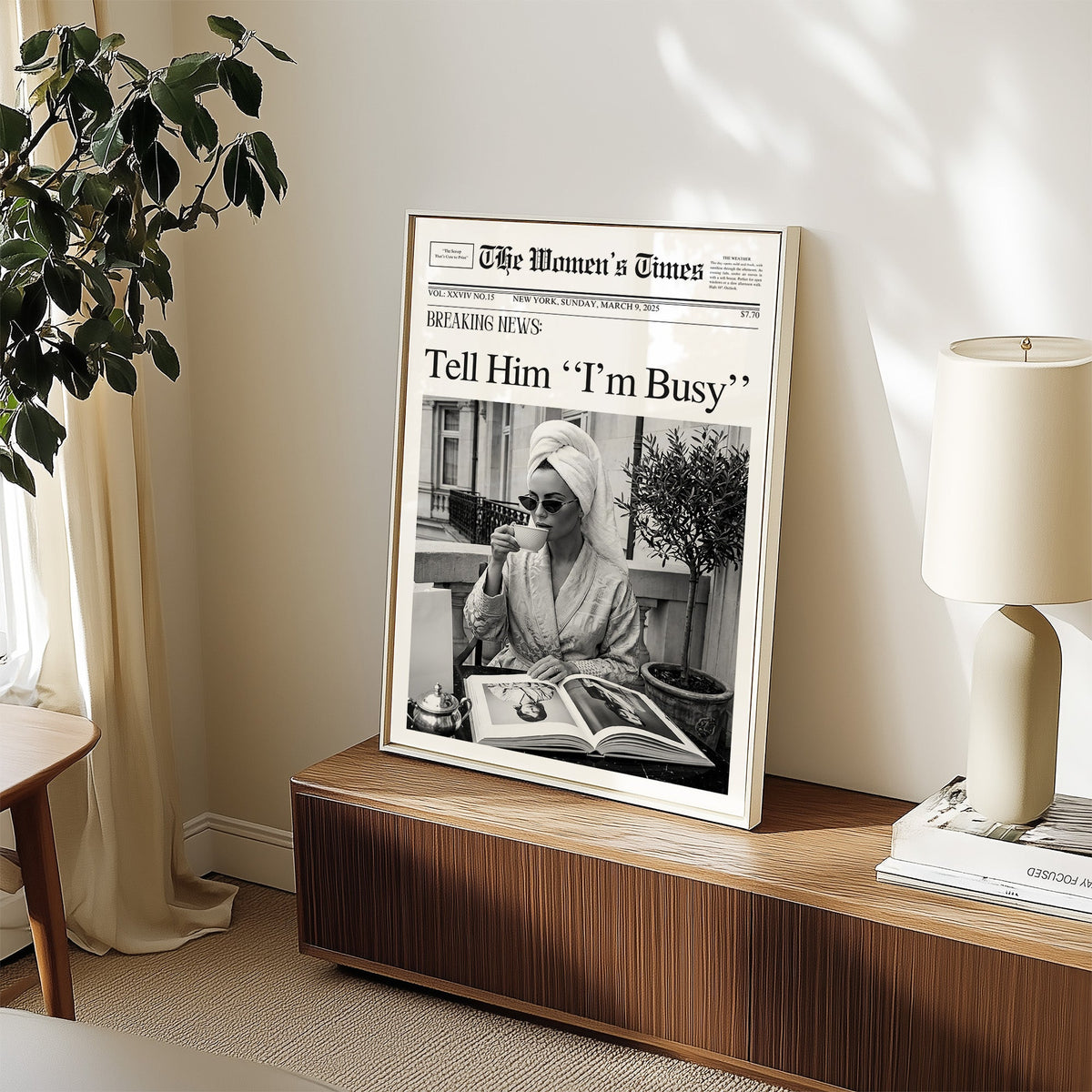 Woman with tea and photo book on balcony newspaper print in a white frame on a walnut sideboard beside a ceramic lamp